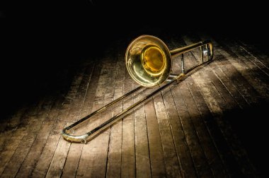 golden brass instrument trombone lies on a dark brown wooden stage in the rays of light clipart