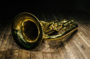 Altın pirinç enstrüman tuba, spot ışıklarının altında kahverengi ahşap bir sahnede yatıyor.