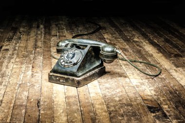 old black colored telephone with a rotary dial stands on a wooden floor in the dark. clipart