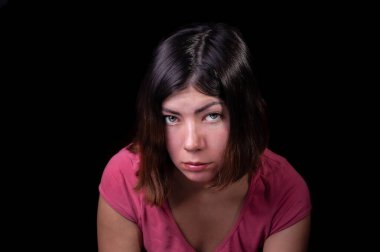 Güzel, koyu saçlı, yeşil gözlü pembe tişörtlü, izole edilmiş siyah bir arka planda üzgün üzgün bakan bir kız.