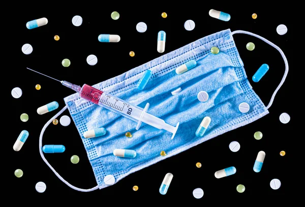 青い外科用フェイスマスクのフラットレイ 赤い液体 と黒の背景に様々なカラフルな丸薬 錠剤やカプセルでいっぱい医療用プラスチック5ミリリットル注射器 トップ表示 — ストック写真