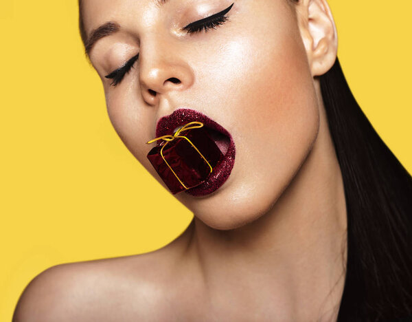 Молодая женщина с подарочной коробкой во рту
