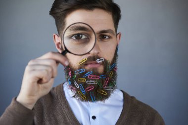 Büyüteç ve kağıt kırpmak içinde sakal gri arka plan üzerinde olan adam yakışıklı portresi sakallı