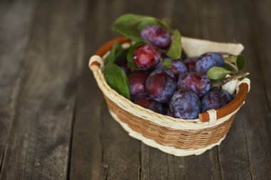 Ahşap masa üzerinde hasır sepet içinde yeşil yaprakları ile taze Erik