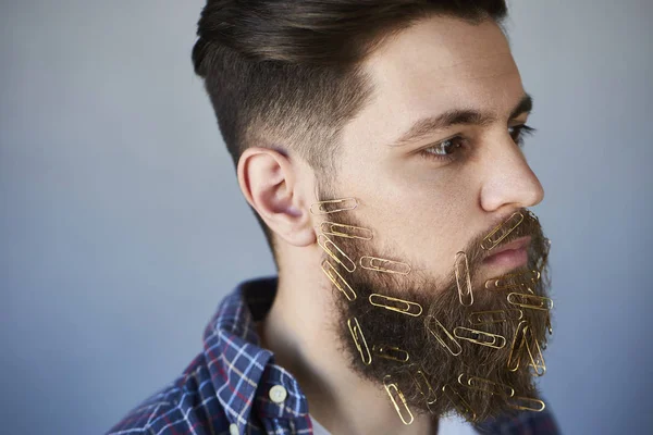 Closeup of young man face with paper clips on beard, gray studio background