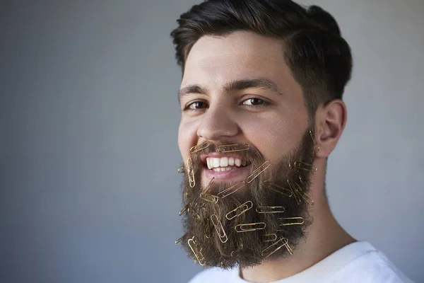 Closeup of young man face with paper clips on beard, gray studio background