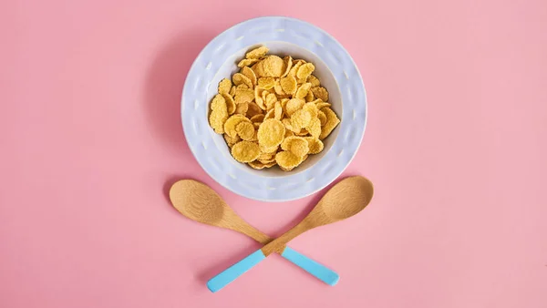Blue plate of cereals and spoons on pink background, top view