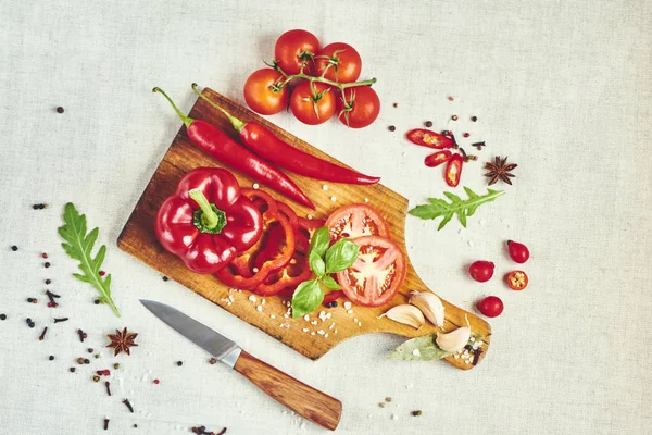 Kesme tahtası, baharat, fesleğen, roka, domates ve bıçak, üstten görünüm ile doğranmış kırmızı biber