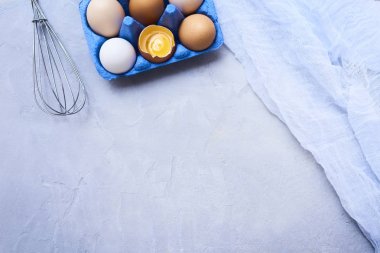 Taze çiğ tavuk yumurta çırpma teli ve tülbent ile mavi karton kutuda yakından görmek mavi beton zemin üzerine.