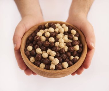 Beyaz arka plan üzerinde izole kahverengi ve beyaz mısır gevreği ile ahşap kase holding erkek eller