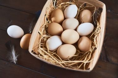 Ahşap kutusunda saman ve ahşap arka plan tüyler ile taze tavuk yumurta.