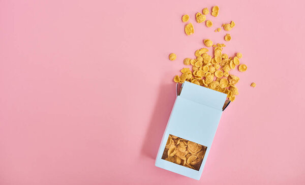 Вид сверху голубой коробки из кукурузных хлопьев на розовом фоне
