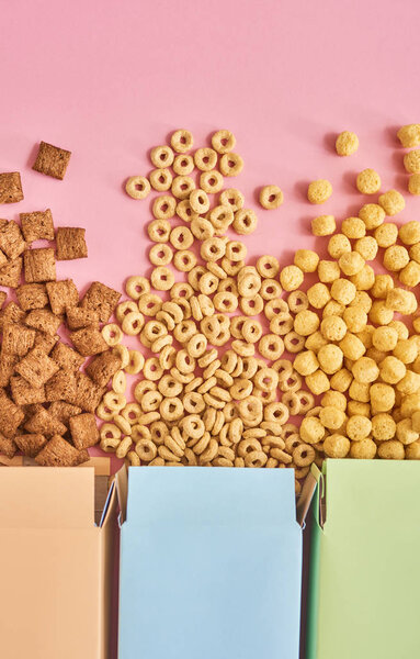 Верхний вид красочных коробок с различными типами кукурузных хлопьев на розовом фоне
