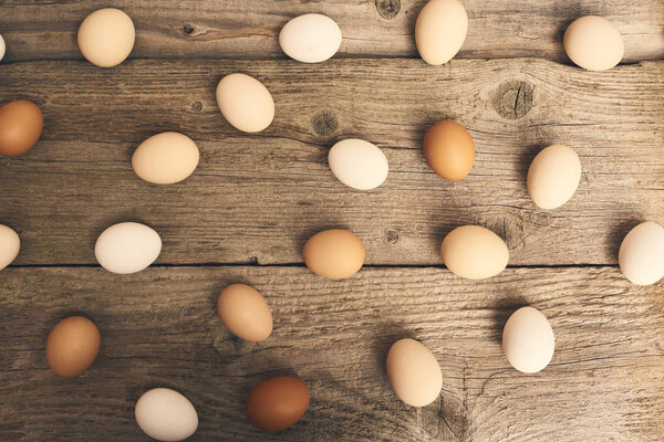 Close-up view of chicken fresh raw eggs over bright brown wooden table background.