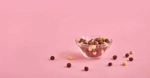 Glass bowl with beige and brown round cornflakes on pink background