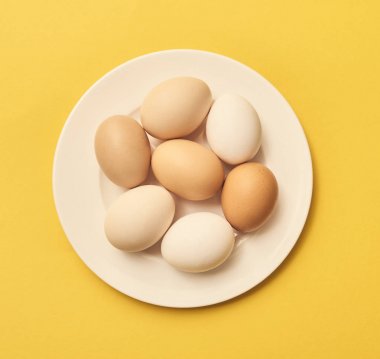 Sarı zemin üzerine beyaz tabakta üstten görünüm taze çiğ tavuk yumurta.