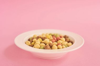 Karışık renkli Mısır gevreği pembe bir arka plan üzerinde beyaz plaka