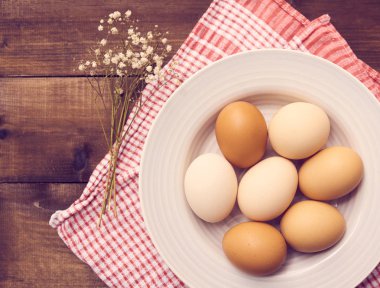 Mutfak havlusu ve çiçeklerle rustik ahşap arka plan üzerinde beyaz tabakta yakın çekim görünümü taze çiğ tavuk yumurta.