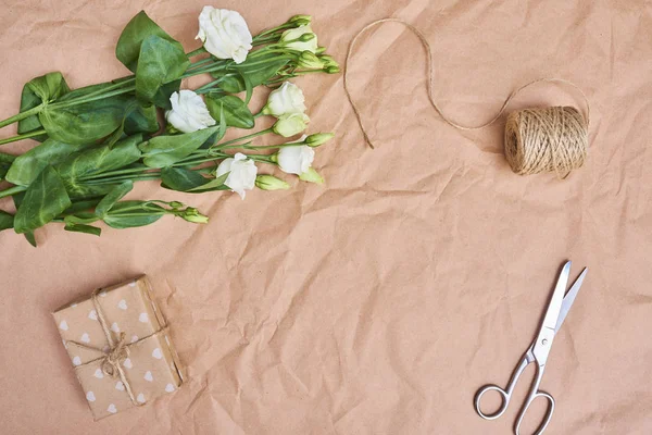 Bahar beyaz eustoma çiçek ve hediye kutusu kahverengi kağıt arka plan, sizin metin için yer ile tebrik kartı. Üstten Görünüm