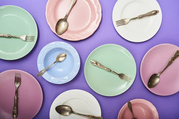 紫の背景に刃物で異なるカラフルな皿のセット — ストック写真