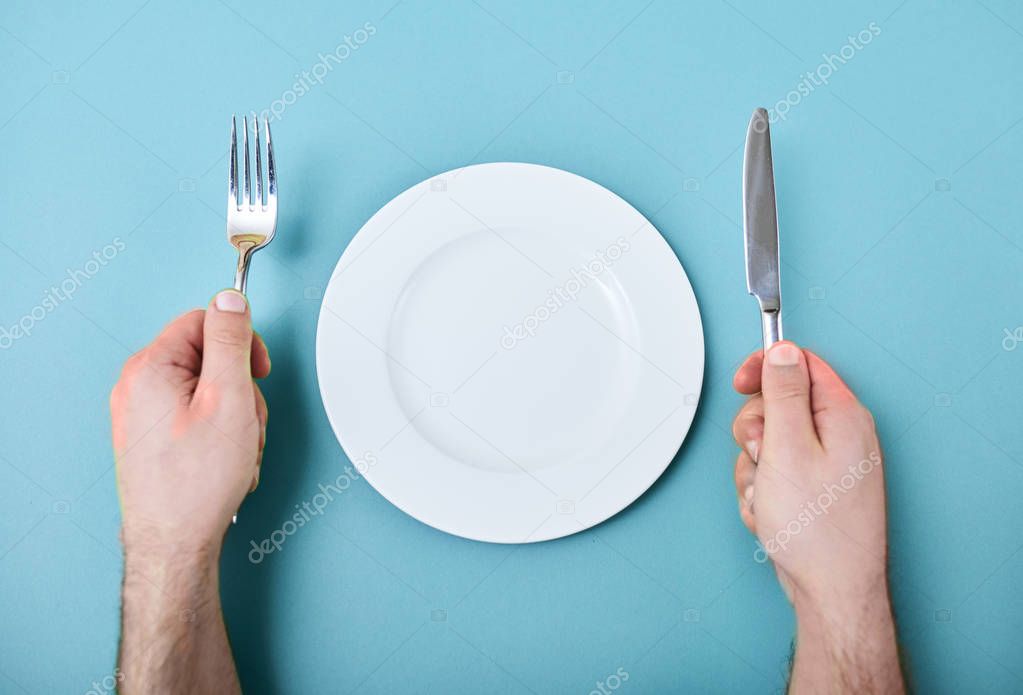 Top view of male hands with cutlery and empty round plate on table
