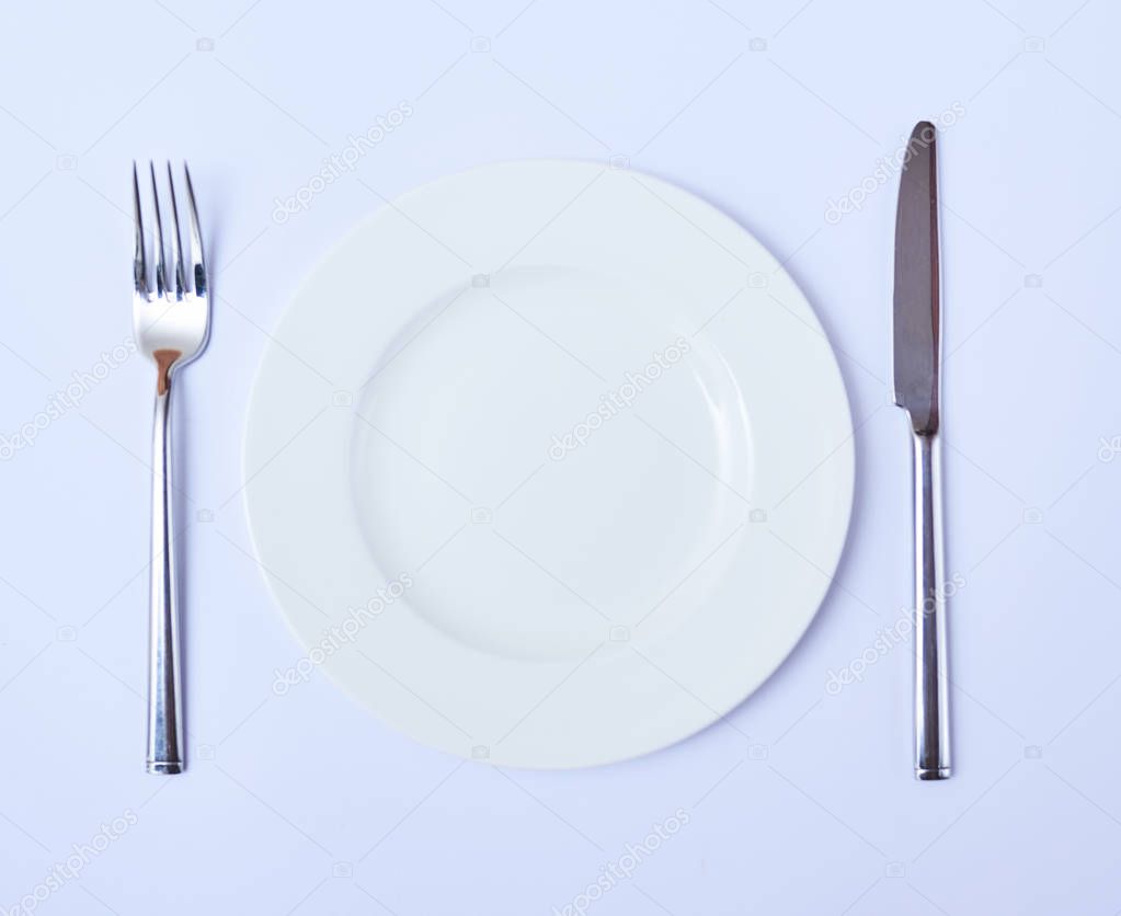 Top view of empty round plate with fork and knife. Restaurant table appointments