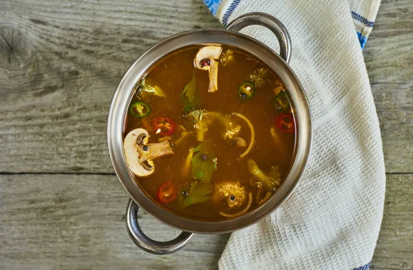 Homemade soup with vegetables and mushrooms in metal pan on wooden table background
