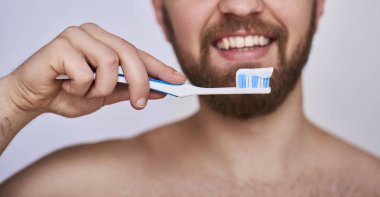 Diş fırçası olan adam. Diş macunu ile diş fırçası tutan ve gri arka plan karşı dururken gülümseyen genç adam Resim kırpılmış