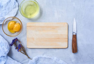 Ayrı yumurta beyaz ve sarısı cam kase boş kesme tahtası, bıçak ve çiçekler ile mavi Beton taş veya mermer üzerinde. Üstten Görünüm. Senin metin için yer.