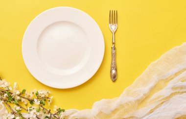 Sarı arka plan üzerinde çatal ve beyaz çiçekli yuvarlak beyaz boş levha. Üstten Görünüm