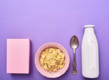 Hububat pembe kase, kaşık, süt ve pembe kutusunun mor arka plan üzerine şişe. Üstten Görünüm