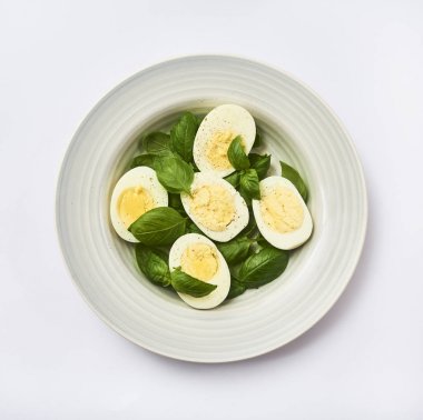 Beyaz arka plan üzerinde izole plaka bırakır haşlanmış yumurta ve taze fesleğen ile lezzetli bir salata yemek için hazırlanıyor