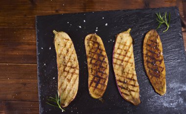 Koyu kahverengi rustik ahşap arka plan üzerinde siyah arduvaz plaka üzerinde sırlı patlıcan ızgara. Üstten Görünüm