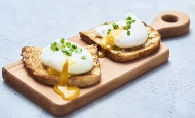 Yakın çekim görünümünü bir lezzetli haşlanmış yumurta ekmek kesme tahtası üzerinde üzerine taze fesleğen yaprakları ile sıvı yumurta sarısı ile mavi Beton taş veya mermer arka plan üzerinde