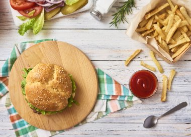 Taze lezzetli hamburger hazırlanması. Kola Beyaz ahşap zemin üzerine yeşil çiğ sebze kesme tahtası ve plaka, patates kızartması ve cam buns. Üstten Görünüm