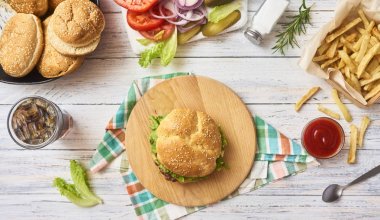 Taze lezzetli hamburger hazırlanması. Kola Beyaz ahşap zemin üzerine yeşil çiğ sebze kesme tahtası ve plaka, patates kızartması ve cam buns. Üstten Görünüm