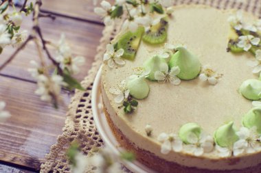 Lezzetli bir cheesecake görünümünü yakın çekim dekore edilmiş merenga, kivi ve beyaz minik çiçekler ile koyu kahverengi ahşap arka plan üzerinde