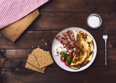 Pastırma, domates, fesleğen ve mantar beyaz tabak, crispbread ve koyu kahverengi rustik ahşap arka plan üzerinde çatal ile lezzetli omlet. Üstten Görünüm