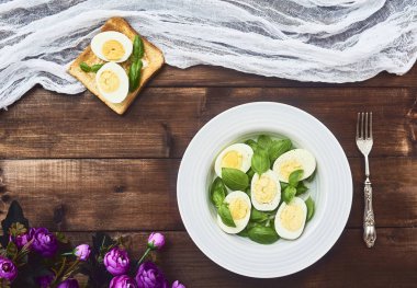 Lezzetli salata ile haşlanmış yumurta ve koyu kahverengi ahşap rustik arka plan üzerinde plaka gevrek ekmek ve mor çiçekler taze fesleğen yaprağı. Üstten Görünüm
