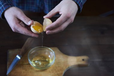 Ayrı yumurta koyu kahverengi ahşap masa üzerinde. Beyaz yumurta sarısı ayıran adam.