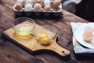 Ayrı yumurta beyaz ve sarısı cam kase koyu kahverengi ahşap masa üzerinde kesme tahtası üzerinde. Arka plan, yumurta kabukları