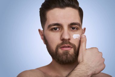 Yüz Nemlendirici olan genç adam. Adam mavi arka plan üzerinde gülümseyen bir fotoğraf. Kendini damat