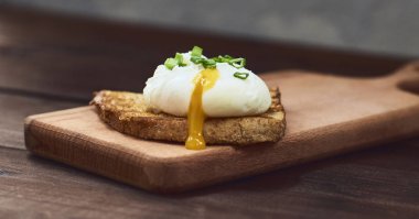 Yakın çekim görünümünü bir lezzetli yumurta ekmek kesme tahtası üzerinde üzerine taze fesleğen yaprakları ile sıvı yumurta sarısı ile koyu kahverengi rustik ahşap zemin üzerinde haşlanmış.