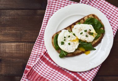 Tasty görünümünü yakın çekim koyu kahverengi rustik ahşap zemin üzerinde tost pembe mutfak havlu ile beyaz tabakta üzerine yumurta taze fesleğen yaprakları ile sıvı yumurta sarısı ile haşlanmış yumurta. Üstten Görünüm