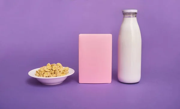 Cereals in pink bowl, bottle of milk and pink box on purple background