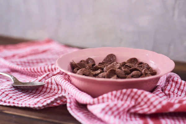 Chocolate cereals in pink bowl, kitchen towel on concrete background