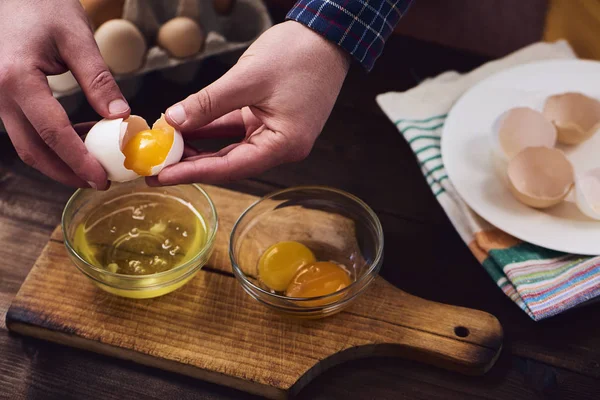 Separated eggs over dark brown wooden table. Man separating yolk from white egg.
