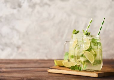Mojito limes ve ahşap masa üzerinde cam kavanozlara nane kokteyli. Beton arka plan. Metin için yer