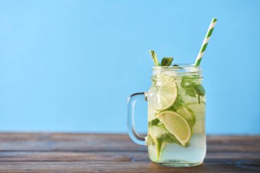 Mojito limes ve ahşap masa üzerinde cam kavanozlara nane kokteyli. Mavi arka plan. Metin için yer