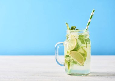 Mojito limes ve ahşap masa üzerinde cam kavanozlara nane kokteyli. Mavi arka plan. Metin için yer